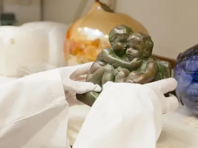 White gloved hands holding a sculpture of two child figures