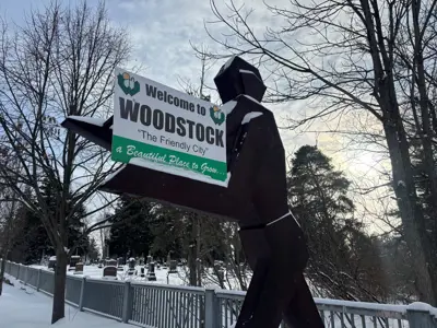 Statue of a human figure holding a Welcome to Woodstock sign